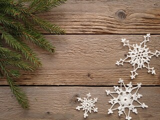 Top view of some  spruce branches and hand-crocheted white snowflakes on a wooden table.