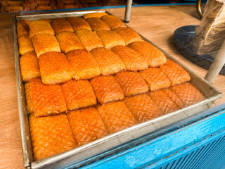 Traditional sweet pastries displayed on metal tray with golden syrup surface in bakery shop. Food culture, dessert preparation, confectionery tradition and culinary presentation.