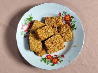 A pile of crispy fried tempeh that looks delicious and tasty, in a glass plate with a floral motif.
