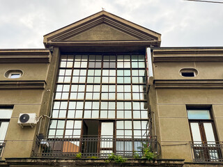 Obraz premium Old building facade with large glass windows framed by geometric grid and metal balcony railings. Architecture, urban design, cultural heritage and city infrastructure.