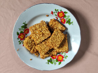 A pile of crispy fried tempeh that looks delicious and tasty, in a glass plate with a floral motif.