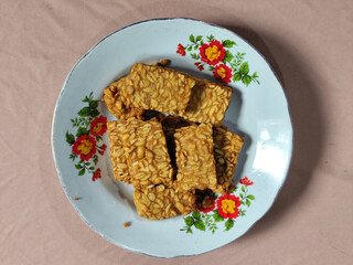A pile of crispy fried tempeh that looks delicious and tasty, in a glass plate with a floral motif.