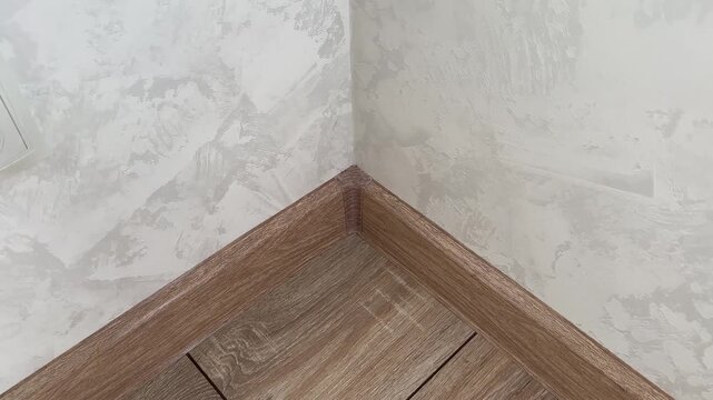 Plastic inner corner of the floor skirting board. Floor skirting boards with wooden texture. White wall