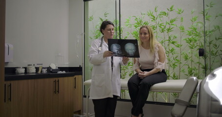 Obraz premium Medical professional showing brain X-ray to middle-aged woman patient during diagnostic consultation in clinic with green bamboo background