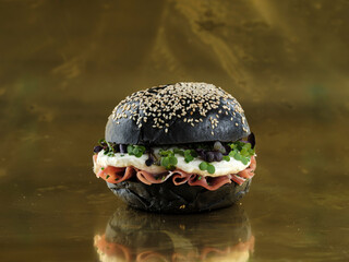 a black burger with sesame seeds, filled with prosciutto, a perfectly fried egg, and vibrant microgreens. It's set against a reflective golden background