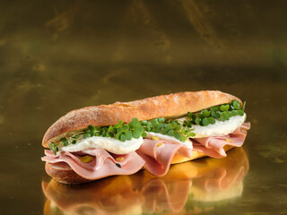 A crispy baguette sandwich filled with tender mortadella, creamy burrata, and vibrant microgreens sits atop a reflective gold surface, radiating culinary allure