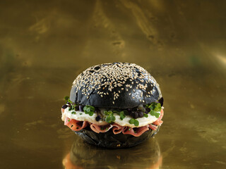 A dark bun burger topped with sesame seeds presents layers of flavor ham, egg, and microgreens. The...