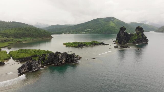 Wide aerial panorama of Poule de Hienghene rock formations, lagoon waters and lush tropical surroundings in New Caledonia.