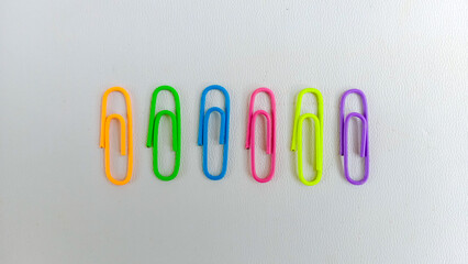 Colorful paperclips in assorted neon shades arranged on a white background, representing stationery...