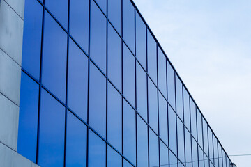 Obraz premium The building's façade is made of blue glass, creating the effect of reflecting the sky. Straight lines and strict forms emphasize the modern style of architecture.