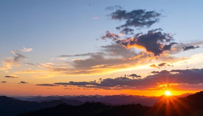 Obraz premium Vibrant sunset over a mountainous landscape, clouds ablaze with orange and yellow hues