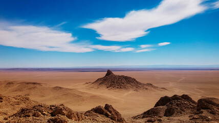Fototapeta premium Vast Desert Landscape with Rocky Outcrop Under Blue Sky