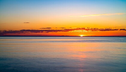 Obraz premium Stunning ocean sunset paints sky with vibrant orange and golden hues reflecting on calm water
