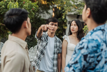 A protective young Southeast Asian man confronts two smug bullies after witnessing them harass his distressed girlfriend, pointing at them angrily with frustration and disbelief.