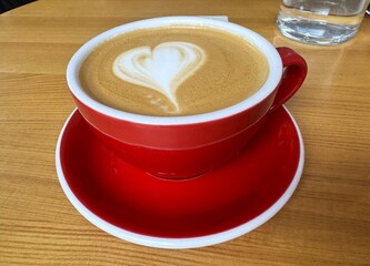 Red cup of cappuccino on the table in a cafe, close up