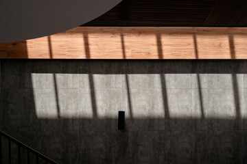 Abstract architectural detail of a modern interior with sunlight casting linear shadows across a textured concrete wall and a wooden ceiling beam.
