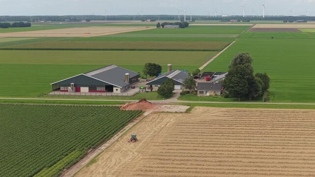 Farm tractor working tilled field, farmhouse and silos in view, Netherlands