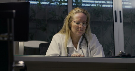 Female doctor lowering head in despair showing signs of severe burnout during nighttime inside...