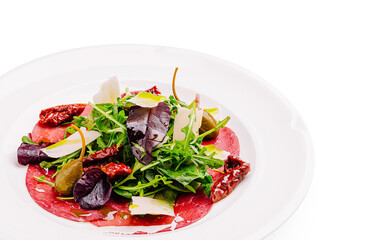 Fresh salad with arugula, dried tomatoes, and slices of carpaccio on a plate