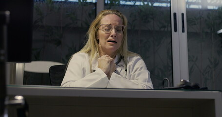 Female doctor lowering head in despair showing signs of severe burnout during nighttime inside...