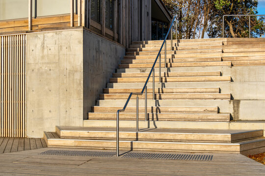 Modern outdoor staircase with concrete walls, wooden steps, and a metal handrail in contemporary architectural design. Concept of urban architecture, construction materials, minimalist public space - Powered by Adobe