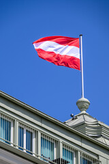 Austrian flag waving on a building rooftop against a blue sky