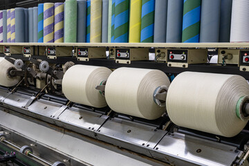 Spools of industrial yarn arranged on racks in a textile manufacturing facility, showcasing synthetic fibers and threads used for fabric weaving, garment production, and clothing industry proce