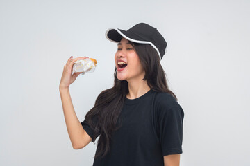 A delighted young Asian woman in a half body shot closing her eyes and opening her mouth, ready to enjoy a burger with a happy expression. Isolated on a white background.