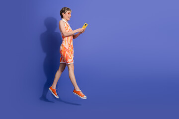Youthful woman with short hair wearing a vibrant summer dress, looking at smartphone, joyful and stylish on vivid purple background