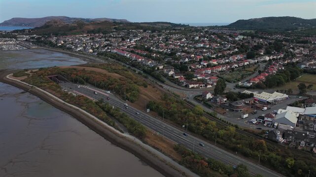 Aerial video of Llandudno Junction and Deganwy across the Conwy estuary, with coastal housing, marina, and a motorway with undersea tunnel. 