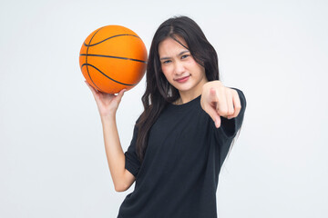 A determined young Asian woman in a half body shot holding a basketball while pointing straight at...