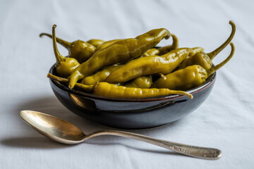 Vibrant Green Peppers in a Black Bowl with Silver Spoon on Soft White Cloth for Culinary Delights