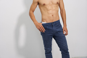 A fit man with a toned physique poses confidently in blue jeans, highlighting his healthy lifestyle and casual yet stylish look.