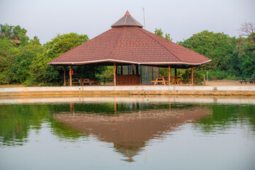 Fototapeta premium A serene and picturesque image of a traditional gazebo by the pond. The roof is reflected beautifully in the calm waters in Lekki Conservation Centre, in Lagos, Nigeria - January 01, 2023