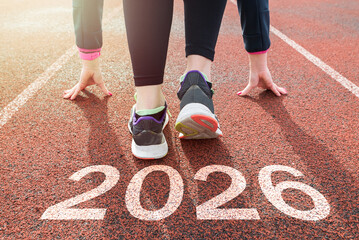 Starting with the new year 2026. a woman prepares to start on an athletics track engraved with 2026. the idea of planning, goals and new year resolutions.