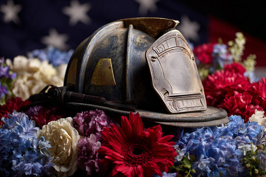 Worn firefighter helmet rests on colorful flowers with a flag backdrop a tribute to fallen heroes