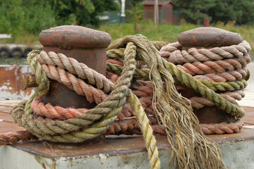 Old weathered mooring ropes wrapped around rusty bollards at a dockside. Nautical detail...