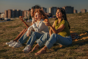 Friends enjoying pizza together at sunset in a park