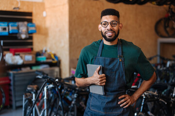 Bicycle shop worker holding tablet and smiling at camera