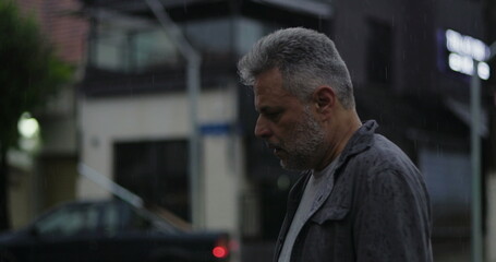 Middle aged man glancing to the side in rain with concerned expression, tense posture and emotional weight in urban street setting