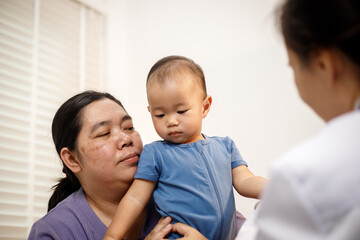 An overweight Asian woman brings her one-year-old son to consult a health expert in a private office. The scene emphasizes family care, professional guidance, wellness improvement