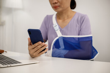 A person in a purple shirt sits at a desk with their right arm in a blue mesh sling, typing on a laptop with their left hand, showing resilience, adaptability, and determination.