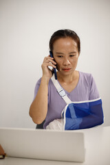 A person in a purple shirt sits at a desk with their right arm in a blue mesh sling, typing on a laptop with their left hand, showing resilience, adaptability, and determination.