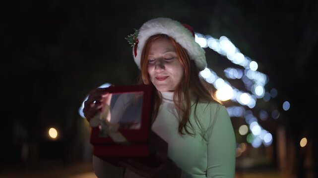 Woman opening glowing Christmas gift box at night with festive lights background