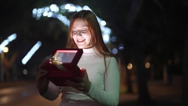 Woman opening glowing Christmas gift box at night with festive lights background