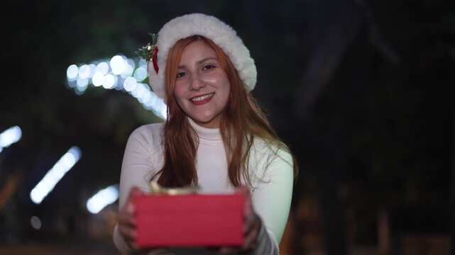 Woman opening glowing Christmas gift box at night with festive lights background