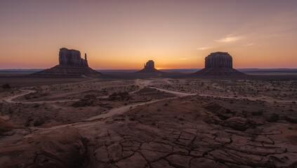 Monument valley landscape with cracked earth and mesas at colorful sunset
