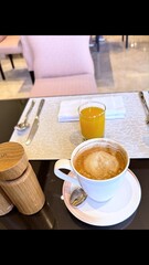 Cappuccino, orange juice, salt and pepper shakers adorning wooden restaurant table, conveying morning comfort and relaxed dining experience