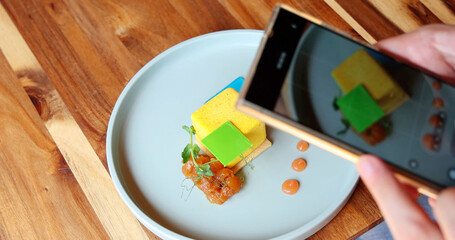 Person photographing gourmet dessert on wooden table with smartphone, capturing modern food presentation and culinary art concept.