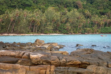 Rocky shoreline with tropical forest and boat on calm sea water